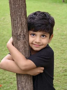 A young boy hugging a tree with a warm smile, symbolizing love for the environme Stock Photos
