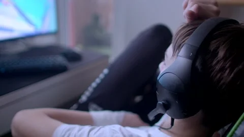 A young boy is immersed in gaming on his computer while wearing a headset in a m Stock Footage 297202833