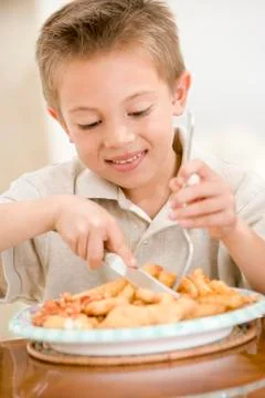 Young boy indoors eating fish and chips smiling Stock Photos