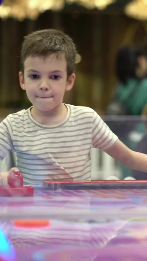 Young boy intently concentrates while playing air hockey on a vibrant colorful Stock Footage 347681734