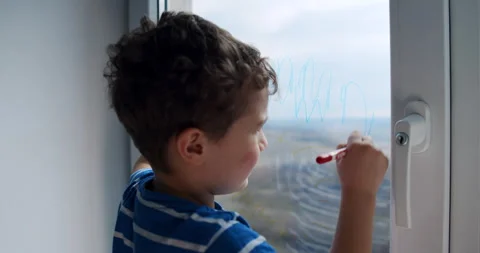 A young boy joyfully draws on a window with a marker, expressing creativity Stock Footage 306673336