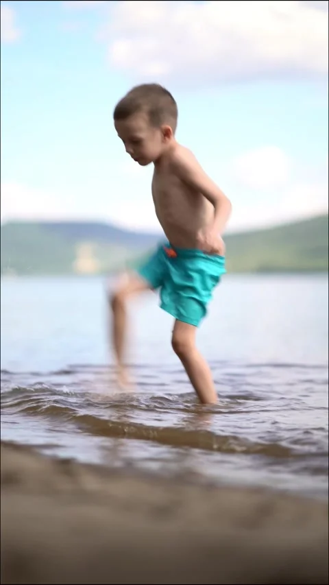 A young boy joyfully kicks and splashes water with his bare foot  Stock Footage 342179378