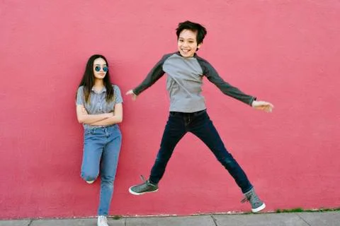 Young Boy Jumps High While His Teen Sister Watches Unimpressed Energetic Stock Photos