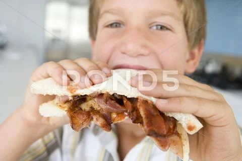 Young boy in kitchen eating bacon sandwich Stock Photos