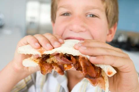 Young boy in kitchen eating bacon sandwich Stock Photos