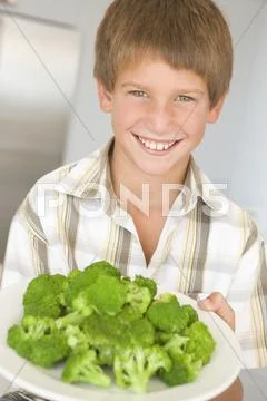 Young boy in kitchen eating broccoli smiling Stock Photos