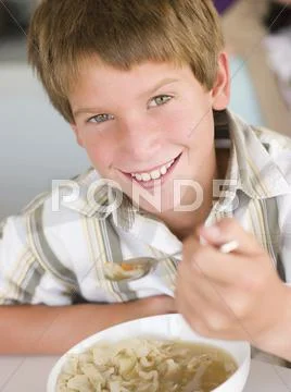Young boy in kitchen eating soup and smiling Stock Photos