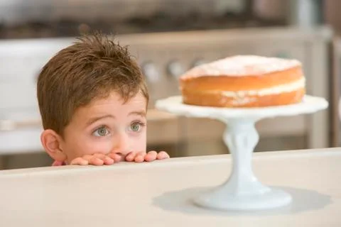 Young boy in kitchen looking at cake on counter Stock Photos