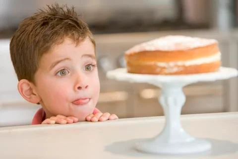 Young boy in kitchen looking at cake on counter Stock Photos