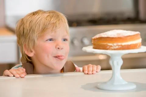 Young boy in kitchen looking at cake on counter Foto stock