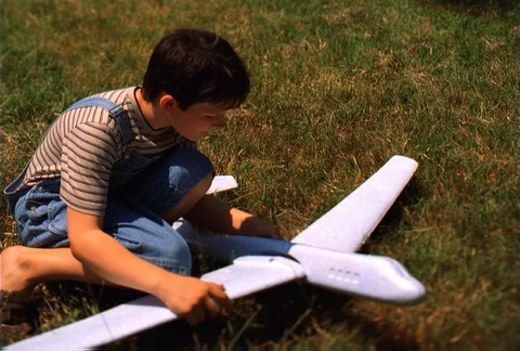 Young boy kneeling on grass while building a toy airplane Video stock 86884387