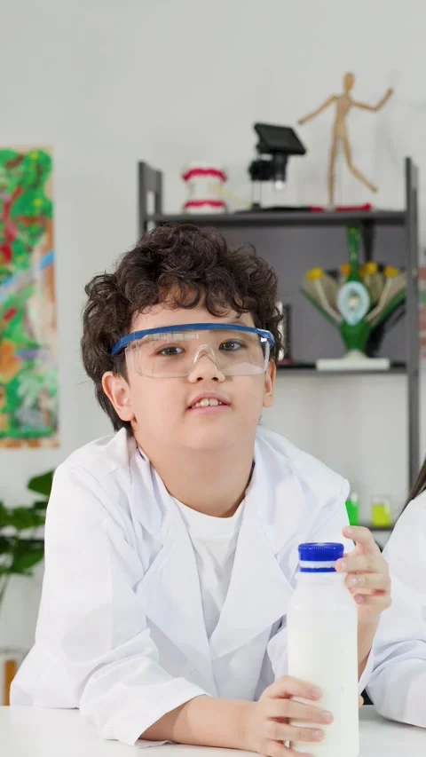 Young Boy in Lab Coat Holding Milk Bottle During Science Experiment Stock Footage 329829348