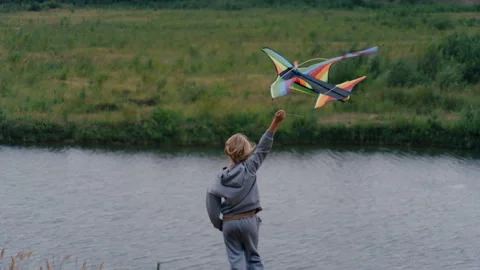 Young boy launching a colorful kite by the lake Stock Footage 344690167