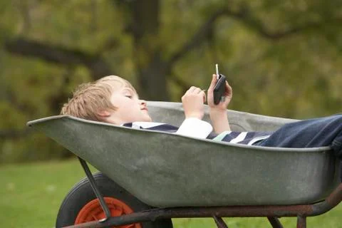 Young boy laying wheelbarrow using smart mobile phone Stock Photos