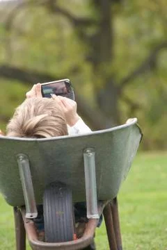Young boy laying wheelbarrow using smart mobile phone Stock Photos