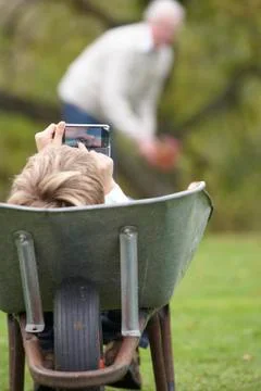 Young boy laying wheelbarrow using smart mobile phone Stock Photos