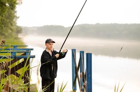 Young boy learning to fish alone on a wooden pier by a misty lake Stock Photos