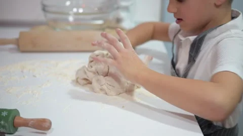 Young boy learning how to knead dough on a table full of flour Stock Footage 324558505