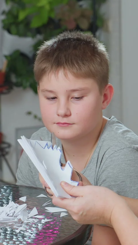 Young boy learns paper snowflake making skills, Caucasian boy patiently observes Stock Footage 330799503