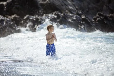 Young boy looking at big waves while standing in shallow water in rough sea Stock Photos