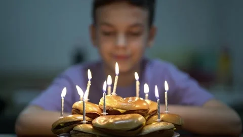 Young boy looking at a birthday cake made from stacked cheeseburgers with lit 動画素材 348790198