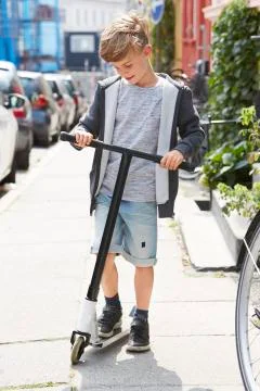 Young boy looking down at scooter on sidewalk. Stock Photos