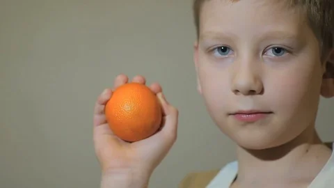 Young boy looking happy at camera and keep a mandarin. Slow motion. Stock-Footage 73717583