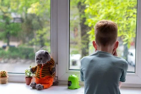 Young boy looking at window. He is sad and unhappy. Self isolation, stay at home Stock Photos