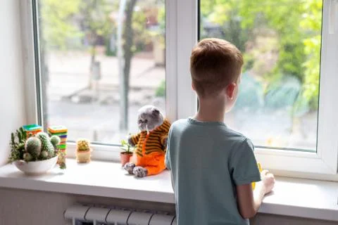 Young boy looking at window. He is sad and unhappy. Self isolation, stay at home Stock Photos