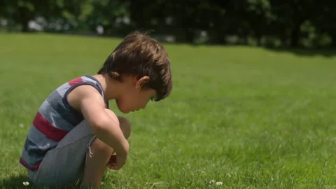A young boy looks down at the green grass, jumps up and runs to his mom Video stock 143621444