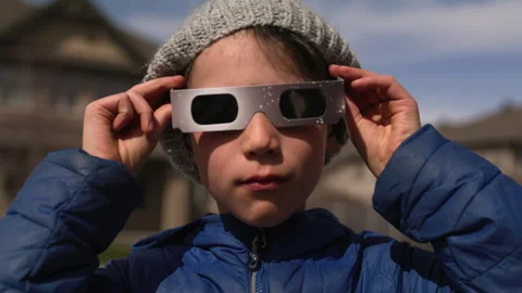 Young boy looks towards camera and puts on solar eclipse glasses to look at s Stock Footage 271315350