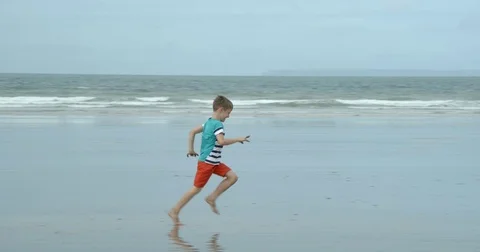 A young boy looks wherehe is running along a beach. Vídeo Stock 79793536