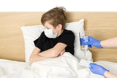 A young boy lying on the bed is given pills and a glass of water. masked boy for Stock Photos
