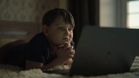 Young boy lying comfortably on bed, watching laptop screen with intense Stock Footage 312721793