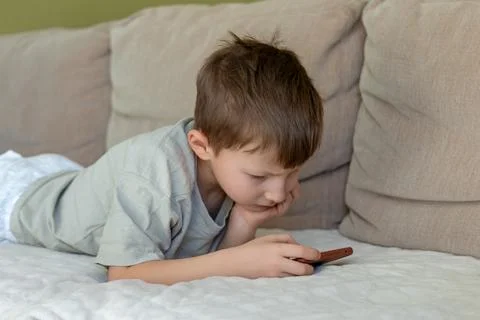 Young Boy Lying on Couch Using Smartphone. A young boy lies on a cozy couch Stock Photos
