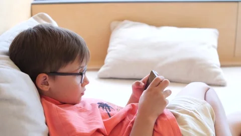 Young boy lying down playing game on cell phone Stock Footage 281971516