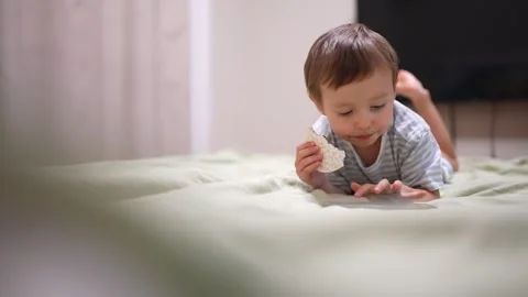 The young boy is lying on the green bed while holding a rice cake, focused on Video stock 320504538