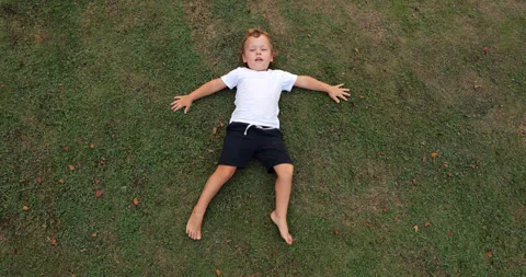 Young boy lying on his back on short green lawn, move hands and legs a bit Stock Footage 322045797