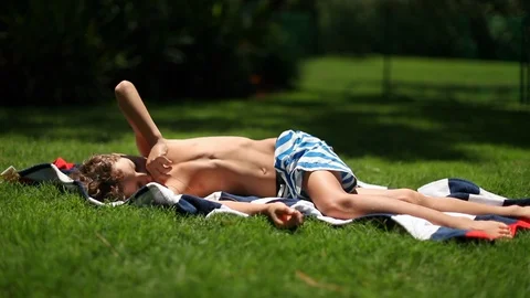 Young boy lying outside in home garden lawn. Child lies outdoors sunbathing Stock Footage 127239054