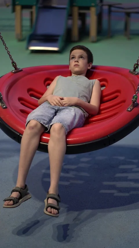 Young boy lying on a red circular swing in a playground Stock Footage 341410042