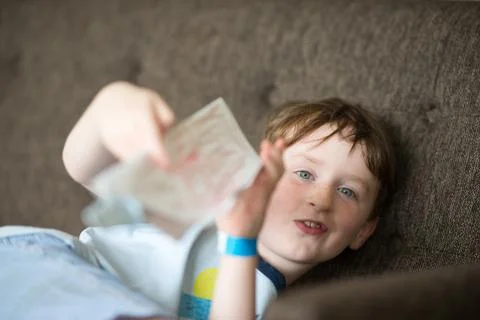 Young boy lying relaxing on a sofa while reading Stock Photos