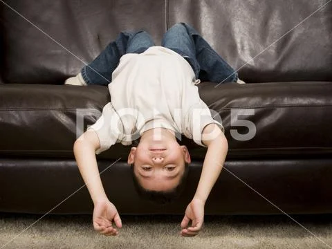Young Boy Lying Upside Down On A Leather Sofa