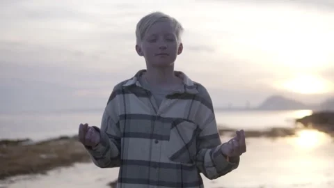 A young boy is meditating on the beach at sunset Stock Footage 268822310