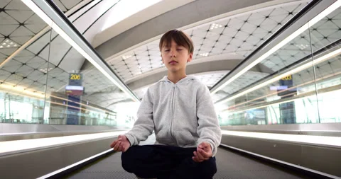 Young boy meditating in the lotus position on a moving walkway Vidéo 324861927