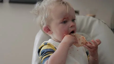 Young boy messy eater eating pizza in a high chair 스톡 동영상 130225505