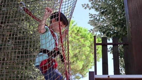 Young boy navigates a climbing net at hanging town on playground Stock Footage 273829297