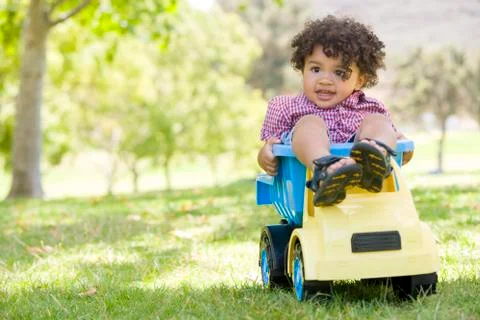 Young boy outdoors playing on toy dump truck smiling Stock Photos