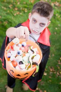 Young boy outdoors wearing vampire costume on Halloween holding candy Stock Photos