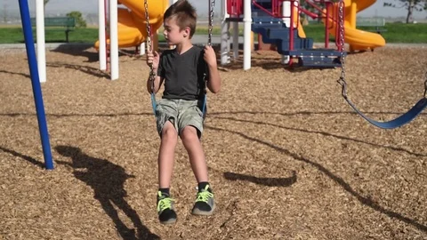 Young boy at park playground by himself, playing, swinging looking sad Stock Footage 94930295