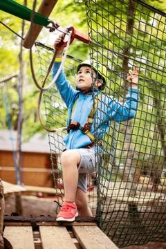 Young boy passing cable route among trees, extreme sport in adventure park Stock Photos
